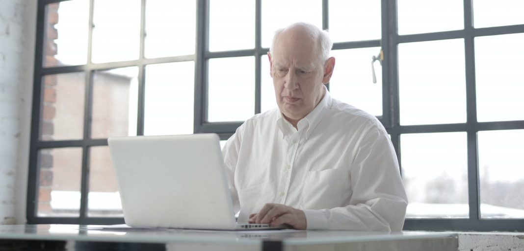 Señor mayor con una camisa blanca usando un macbook